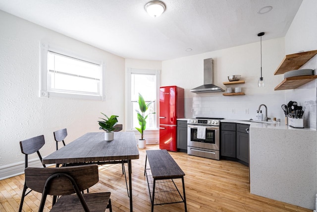 kitchen with pendant lighting, sink, electric range, wall chimney exhaust hood, and light wood-type flooring