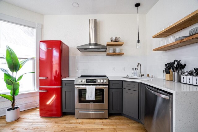 kitchen with wall chimney exhaust hood, sink, gray cabinetry, decorative light fixtures, and stainless steel appliances