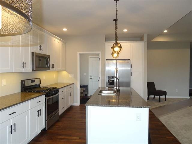 kitchen with appliances with stainless steel finishes, white cabinetry, an island with sink, sink, and dark wood-type flooring