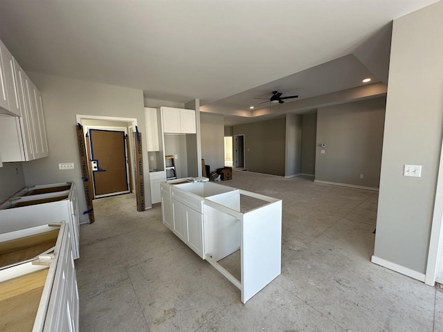 kitchen with a raised ceiling, a ceiling fan, white cabinets, a kitchen island, and baseboards