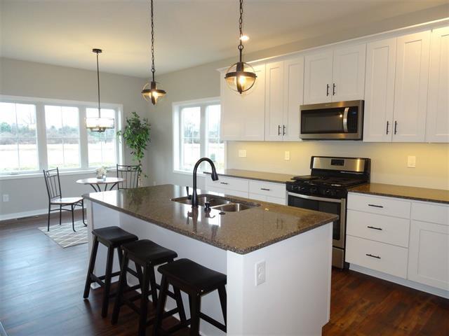 kitchen featuring a center island with sink, appliances with stainless steel finishes, dark wood-type flooring, white cabinets, and a sink