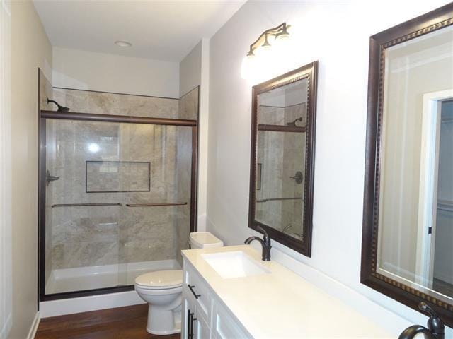 bathroom featuring toilet, a stall shower, wood finished floors, and vanity