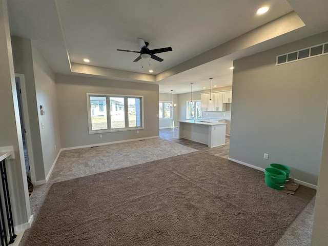 unfurnished living room featuring recessed lighting, visible vents, a raised ceiling, and light colored carpet