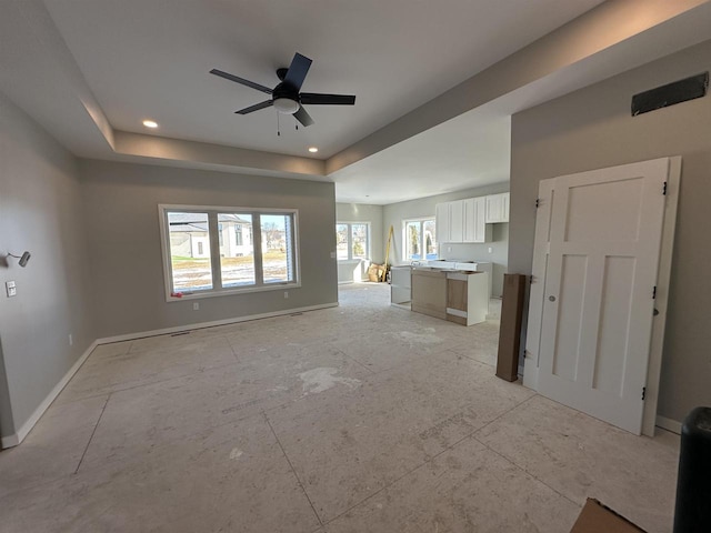 unfurnished living room featuring ceiling fan, recessed lighting, a raised ceiling, and baseboards