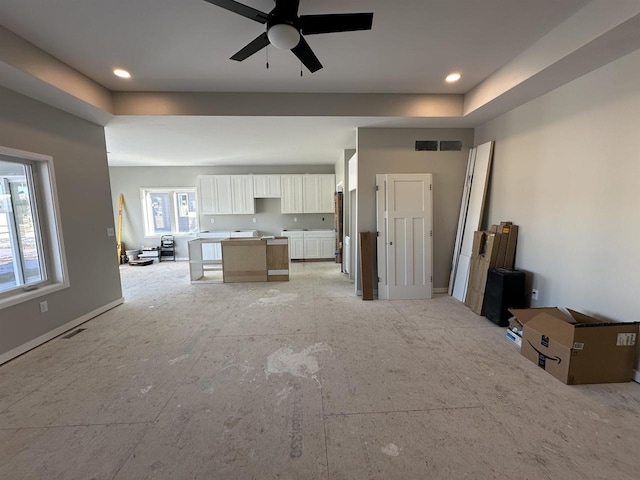 unfurnished living room featuring a raised ceiling, visible vents, and ceiling fan