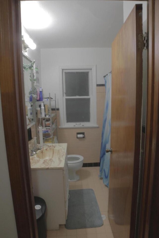 bathroom featuring tile patterned floors, vanity, tile walls, and toilet