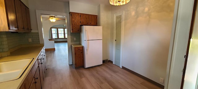 kitchen with decorative backsplash, ceiling fan with notable chandelier, sink, white refrigerator, and light hardwood / wood-style flooring