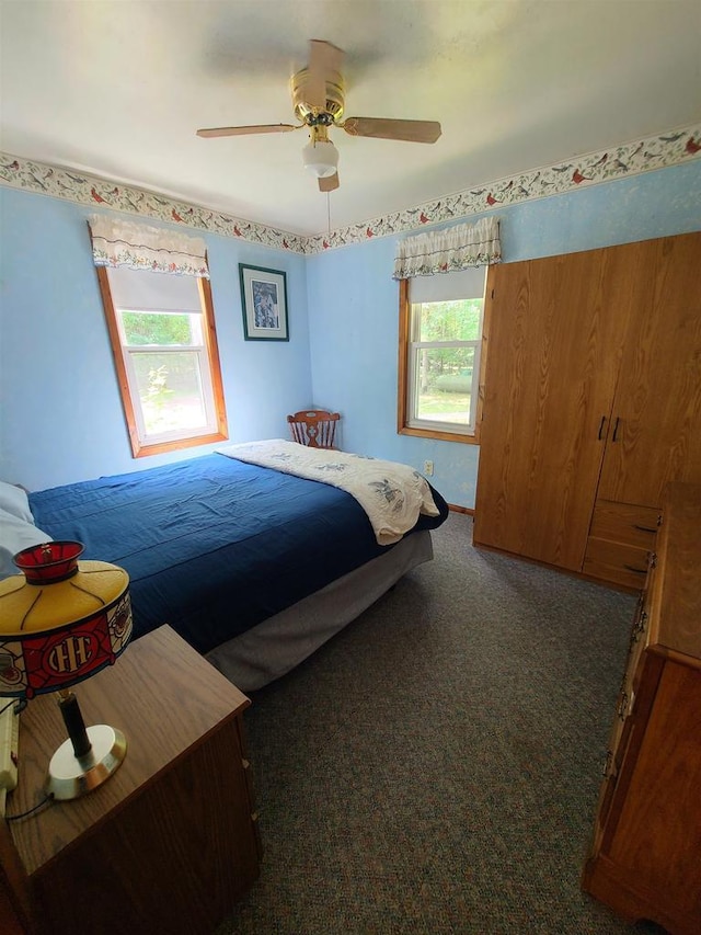 bedroom with multiple windows, dark carpet, and ceiling fan