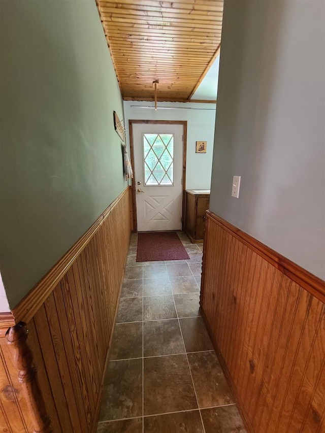 entryway featuring wood ceiling, dark tile patterned floors, and wood walls