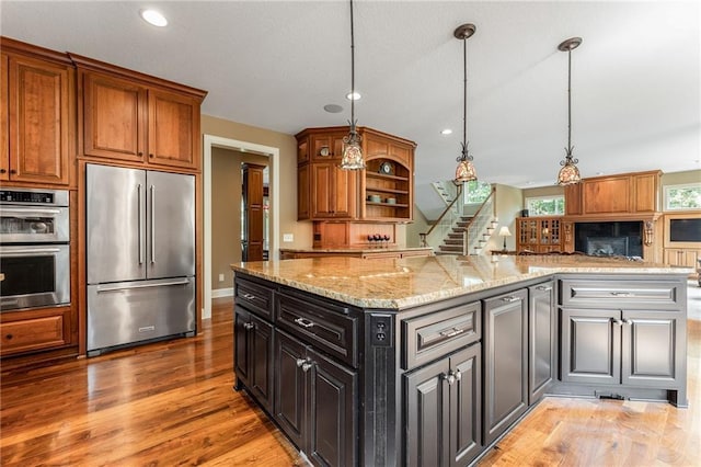 kitchen featuring wood-type flooring, hanging light fixtures, a center island, light stone countertops, and appliances with stainless steel finishes