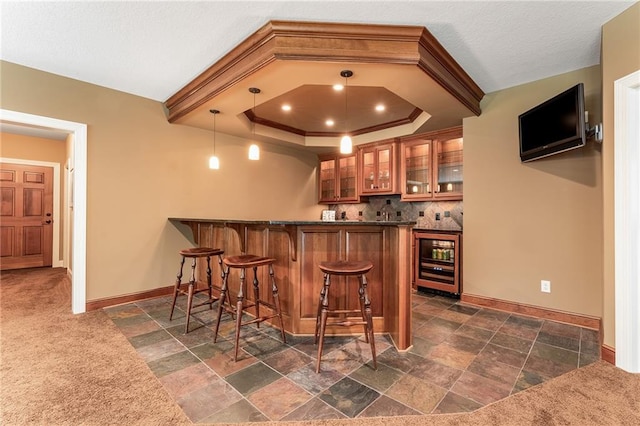 bar with dark carpet, hanging light fixtures, a raised ceiling, decorative backsplash, and wine cooler