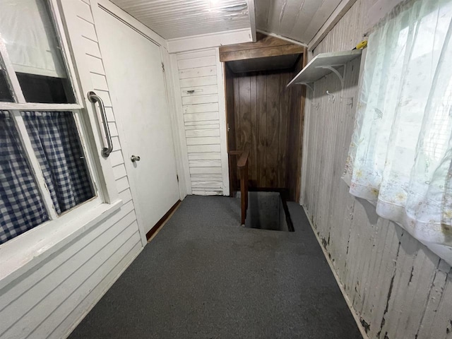 hallway with dark colored carpet, vaulted ceiling, and wooden walls