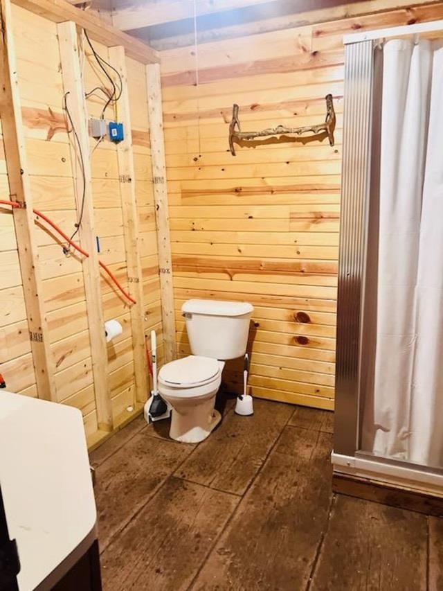 bathroom featuring wood-type flooring, wooden walls, and toilet