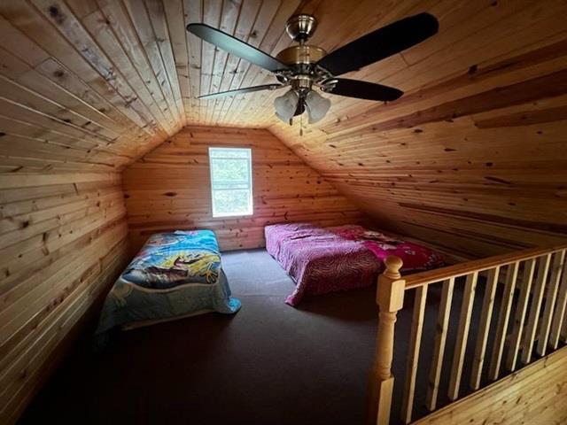 unfurnished bedroom featuring wooden walls, lofted ceiling, ceiling fan, and wooden ceiling