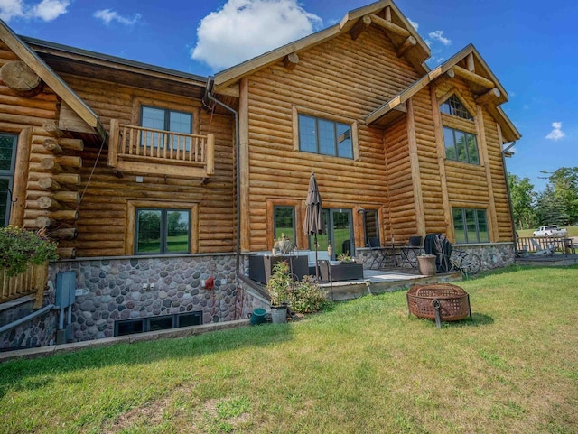 rear view of house with a balcony, a yard, a patio area, and an outdoor fire pit