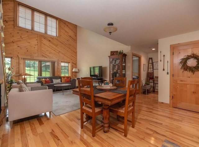 dining area with a high ceiling, light hardwood / wood-style flooring, and wood walls