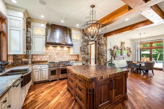 kitchen with custom exhaust hood, a chandelier, hanging light fixtures, double oven range, and a kitchen island