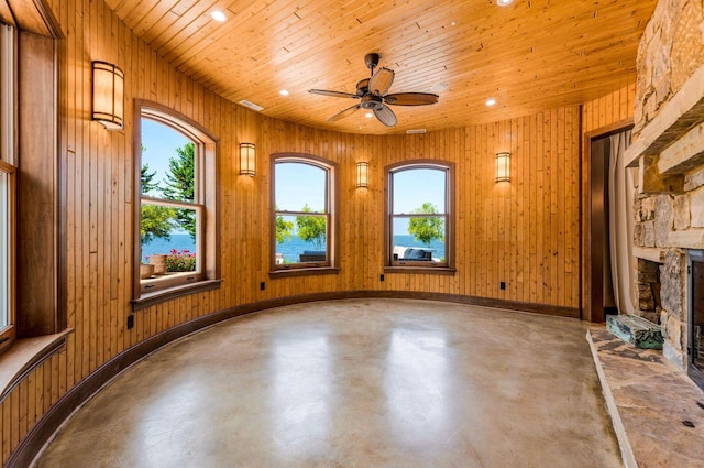 unfurnished living room featuring a stone fireplace, concrete floors, a healthy amount of sunlight, and wood walls