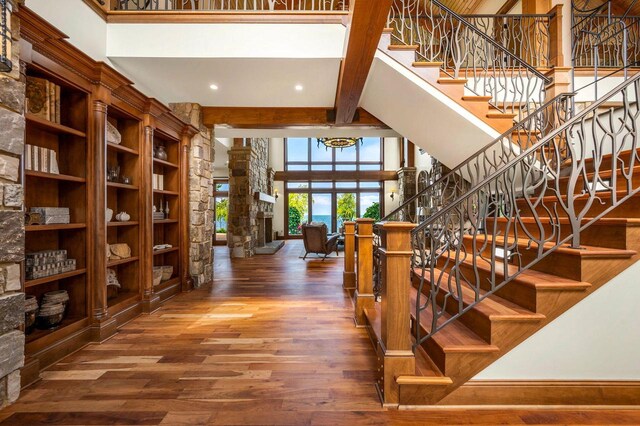 stairway with beamed ceiling, a fireplace, hardwood / wood-style floors, and a towering ceiling