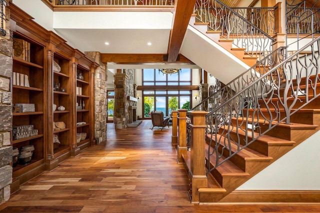 stairway with a stone fireplace, decorative columns, wood-type flooring, a high ceiling, and beam ceiling