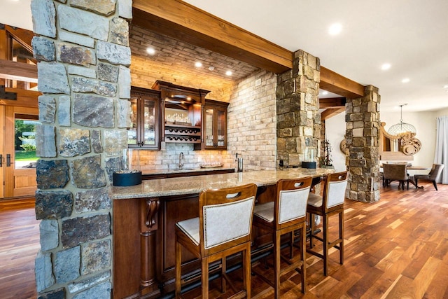 bar featuring sink, ornate columns, dark hardwood / wood-style flooring, beam ceiling, and light stone countertops