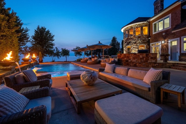 pool at dusk with a patio area, pool water feature, and an outdoor living space with a fireplace