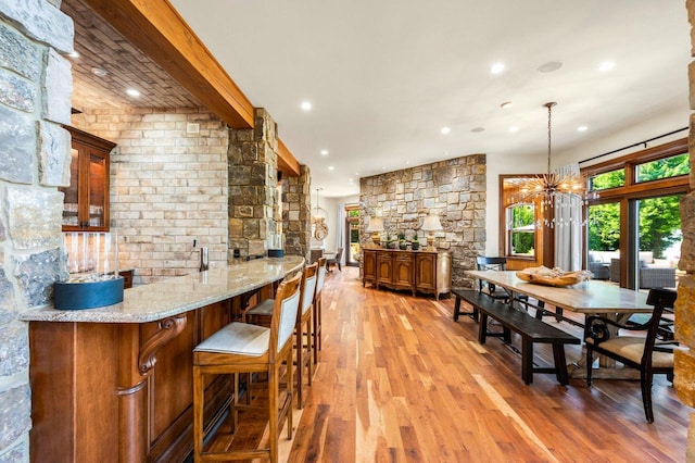 interior space with bar, a notable chandelier, light hardwood / wood-style floors, and beamed ceiling