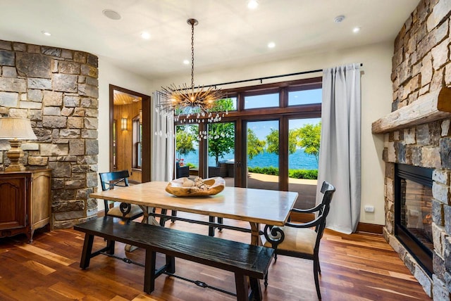 dining area with a water view, dark hardwood / wood-style floors, a stone fireplace, and a notable chandelier