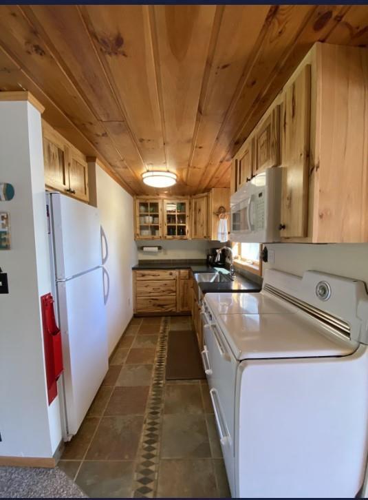 kitchen with light brown cabinets, wooden ceiling, dark tile patterned floors, and white appliances