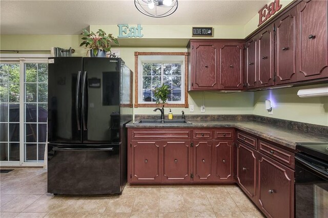 kitchen with light tile patterned floors, a healthy amount of sunlight, sink, and black refrigerator