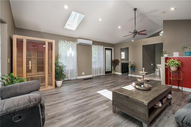 living room with hardwood / wood-style flooring, lofted ceiling with skylight, ceiling fan, and a wall unit AC