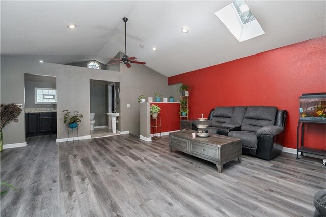 living room featuring a skylight, wood-type flooring, high vaulted ceiling, and ceiling fan