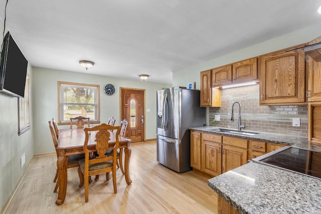 kitchen with sink, decorative backsplash, light wood-type flooring, stone countertops, and stainless steel fridge with ice dispenser