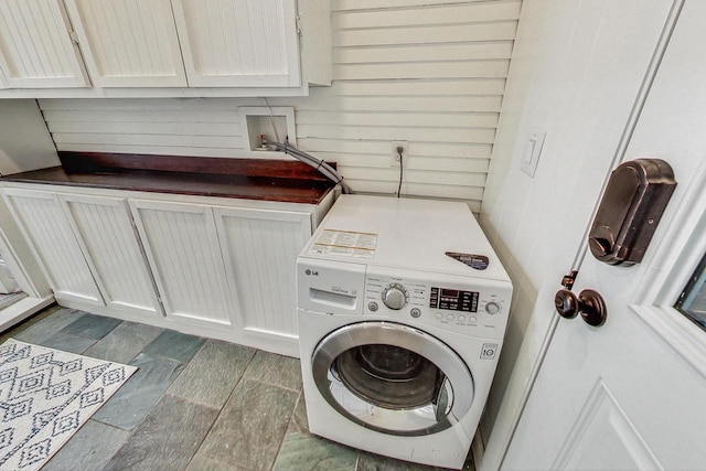 clothes washing area with cabinets, washer / dryer, and wood walls