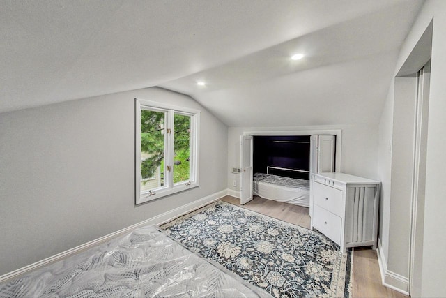 bedroom featuring lofted ceiling, light hardwood / wood-style flooring, and a textured ceiling