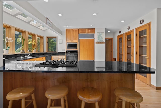 kitchen with dark stone countertops, a breakfast bar, sink, black appliances, and light hardwood / wood-style flooring