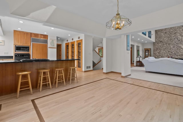 interior space featuring built in appliances, light wood-type flooring, a kitchen breakfast bar, pendant lighting, and a chandelier