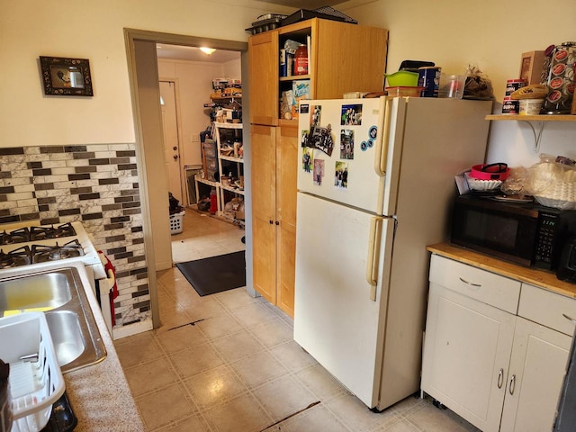 kitchen with light tile patterned flooring, white cabinetry, backsplash, and white fridge