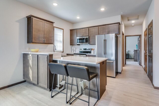 kitchen featuring appliances with stainless steel finishes, light hardwood / wood-style flooring, a center island, and decorative backsplash