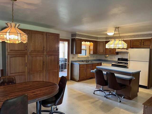 kitchen with pendant lighting, white appliances, backsplash, sink, and exhaust hood