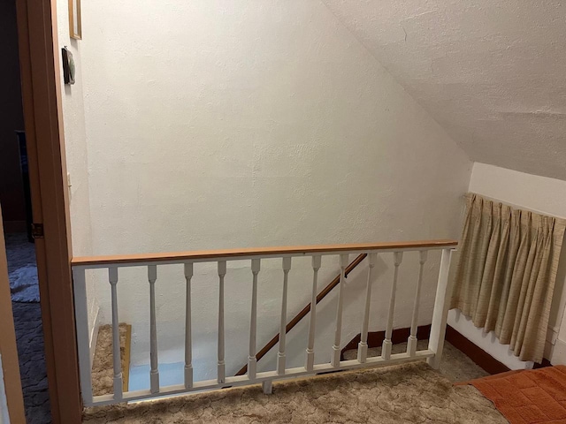 stairway with a textured ceiling, vaulted ceiling, and carpet