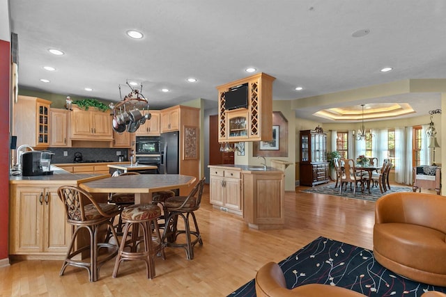 kitchen with black appliances, a raised ceiling, light brown cabinetry, kitchen peninsula, and light wood-type flooring