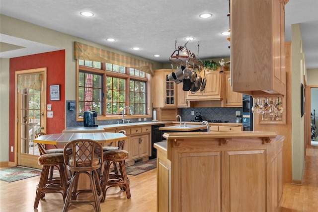 kitchen with black dishwasher, light brown cabinetry, light hardwood / wood-style floors, and kitchen peninsula