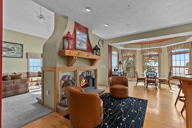 living room featuring ceiling fan, light hardwood / wood-style flooring, and a textured ceiling