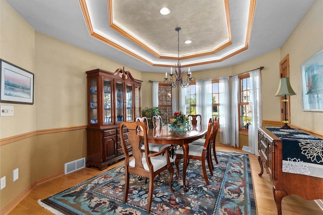 dining area with ornamental molding, a tray ceiling, a chandelier, and light hardwood / wood-style flooring