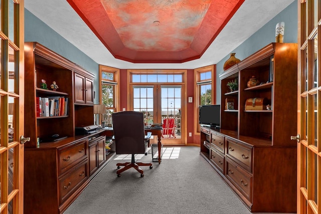 carpeted home office with french doors and a tray ceiling