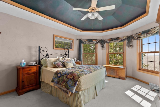 bedroom with ceiling fan, light colored carpet, a raised ceiling, and multiple windows