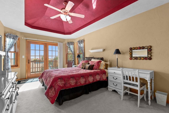 carpeted bedroom featuring access to outside, ceiling fan, and a tray ceiling