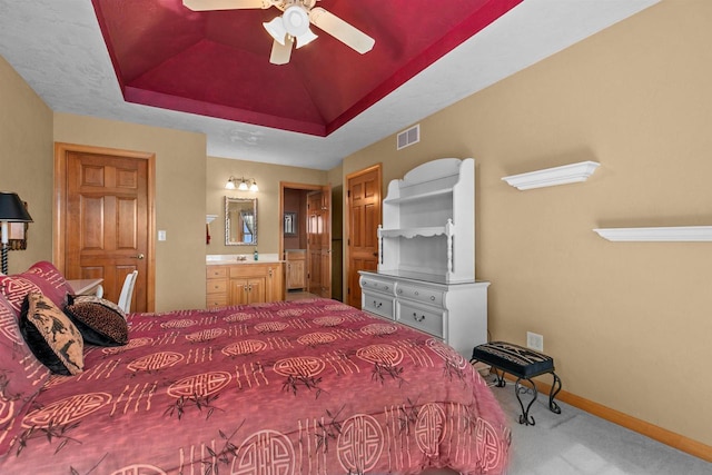 bedroom featuring ensuite bathroom, carpet flooring, ceiling fan, and a tray ceiling