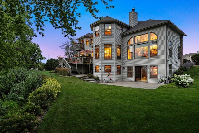 back house at dusk featuring a patio area, a deck, and a lawn